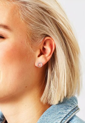 Sølv cirkulært stykke ørering med små klare ædelsten, der har en struktureret overflade og en poleret finish, båret på et kort blonde hår.