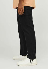 Czarne spodnie cargo wykonane z bawełnianej mieszanki tkanin, wyposażone w boczne kieszenie, zwężane nogawki oraz elastyczne sznurki u kostek, zestawione z białymi tenisówkami.