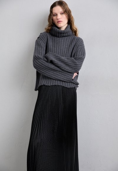 Suéter de gola alta cinza, com riscas, mangas largas e saia preta plissada, apresentando um acabamento texturizado e um corte descontraído.