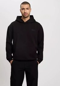 Czarna bluza z kapturem wykonana z miękkiego materiału. Posiada kieszeń kangurzą i mały detal z logo na klatce piersiowej. Luźny krój z długimi rękawami.