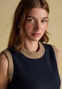 Dark blue sleeveless sweater with a beige ribbed collar and armholes, featuring a textured fabric and a fitted design.