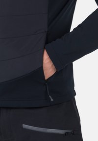 Herrars svart träningsskjorta med en ficka med dragkedja på sidan, slät tyg och ribbade muddar; kontrasterande sömmar längs bålen.