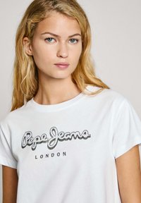 Witte katoenen t-shirt met een ronde hals, korte mouwen en een zwart glitterlogo "Pepe Jeans LONDON" over de borst.