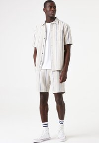 Lichtgekleurde, gestreepte korte mouwen shirt met een zak, gecombineerd met bijpassende shorts. Accessoires zijn witte sneakers en gestreepte sokken.