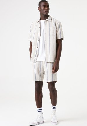Light-colored, striped short-sleeve shirt with a pocket, paired with matching shorts. Accessories include white sneakers and striped socks.