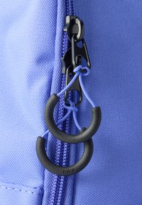 Φερμουάρ σε μωβ ύφασμα τσάντας με μαύρα εξαρτήματα, που διαθέτει λουράκι έλξης με θηλιά και υφή στην επιφάνεια. Το λογότυπο της Nike είναι ορατό στο λουράκι έλξης.