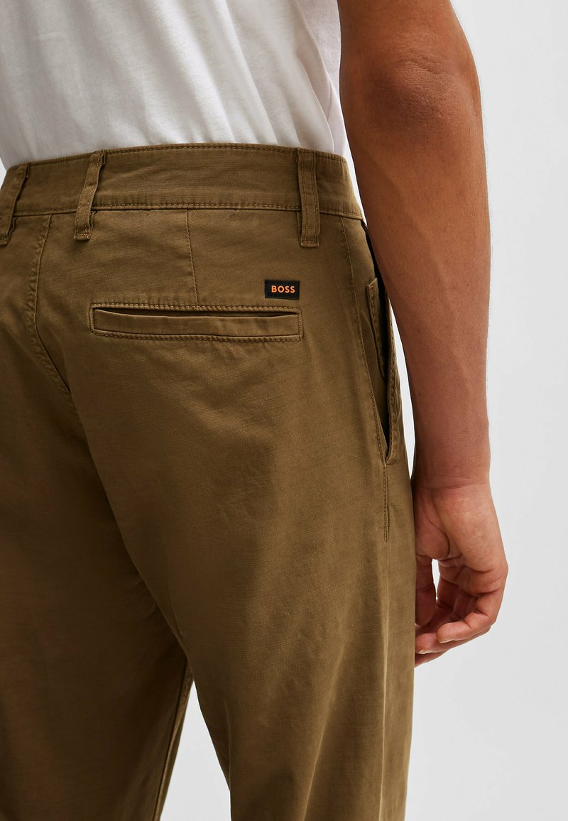 Pantalon en coton marron avec une coupe décontractée, doté d'une poche arrière et d'une petite étiquette "BOSS" noire et orange sur la ceinture.