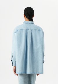 Lys blå denimskjorte, avslappet passform, med rygghals, knapper på ermene, og rett avslutning. Myk tekstur med en falmet overflate.