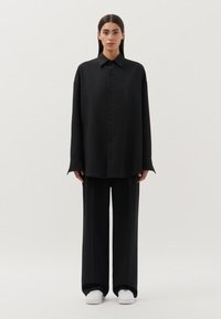 Zwarte oversized button-up shirt met een spitse kraag, lange mouwen en bijpassende losse broek. De stof heeft een gladde textuur.