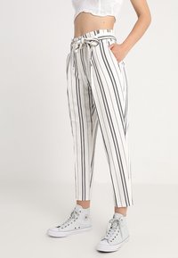 Černobílé pruhované zkrácené kalhoty s páskem v pase, vyrobené z lehké tkaniny, v kombinaci s vysokými teniskami.