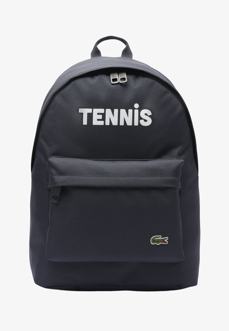 Zaino blu navy con tasca frontale con cerniera, testo "TENNIS" in alto e piccolo logo coccodrillo verde nell'angolo in basso a destra.
