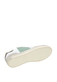 Zapato deportivo blanco con acentos en verde y beige, suela de goma texturizada y parte superior de tela suave que combina diferentes materiales y colores.