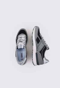 Zapatillas deportivas en gris y negro, fabricadas con materiales de malla y ante, diseñadas con una suela blanca y acentos estampados. Los cordones son blancos.