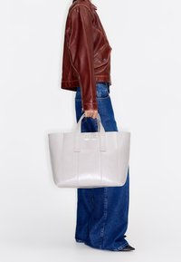 Borsa tote in pelle grigia con due manici, forma rettangolare piatta, texture liscia e cuciture verticali; logo visibile sulla parte frontale.