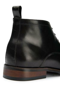Black leather ankle boot with a smooth finish, curved shape, and a brown wooden heel. Includes a pull tab for easy wear.