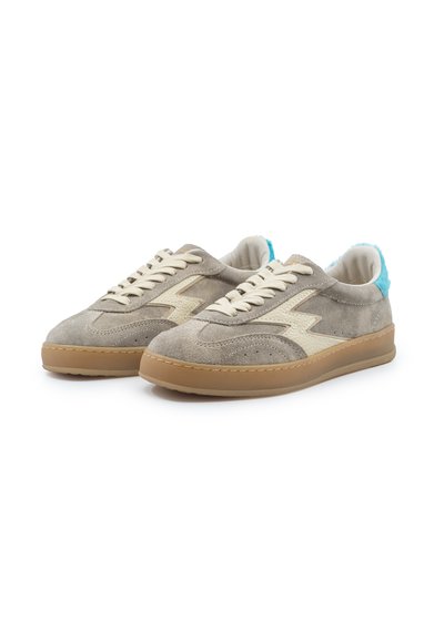 Paire de baskets en daim beige avec un motif d'éclair blanc, des lacets blancs, une semelle gomme et des accents bleu clair au niveau du talon sur fond blanc.