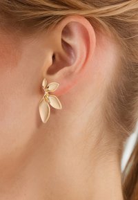 Ohrstecker in Goldoptik mit Blattdesign, die glatte, polierte Blätter und eine geschwungene Form zeigen, am Ohr eines Modells platziert.