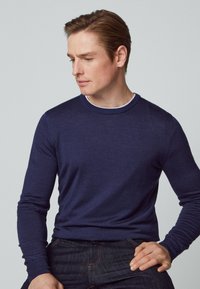 Dunkelblaues Langarm-Sweatshirt aus weichem Material, mit Rundhalsausschnitt und engen Bündchen, kombiniert mit dunklen Jeans.