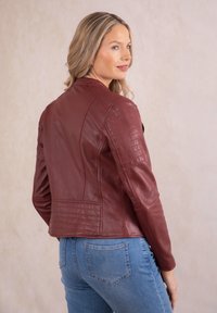 Burgundy leather jacket with quilted shoulder details, fitted design, and a cropped length, paired with light blue jeans.