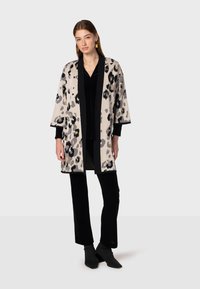 Beige, grijs en zwarte leopardprint kimono. Losse pasvorm met brede mouwen, accentueert door een effen zwarte rand. Gecombineerd met zwarte broek en laarzen.