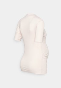 Camiseta de maternidade em rosa claro, com mangas curtas, textura canelada e franzidos nas laterais para um ajuste justo durante a gravidez.