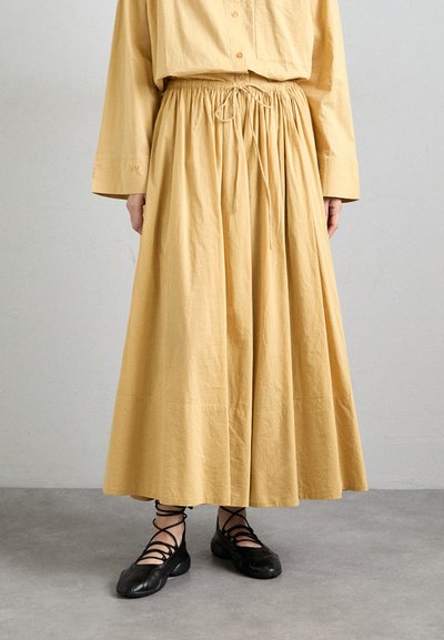 Jupe longue jaune en coton avec une taille élastique et un cordon de serrage. Associée à des chaussures noires à lacets, présentant un design à bout rond.