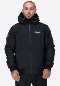 Czarna bluza z zamkiem i kapturem, z elastycznymi mankietami i dołem, z białym logo na klatce piersiowej oraz aplikacją w kształcie flagi Union Jack na rękawie.