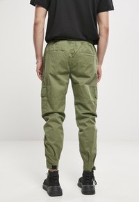 Pantalones de cargo verdes de algodón con un corte relajado, cinturilla elástica, bolsillos laterales y puños ajustados, combinados con zapatillas negras de caña alta.