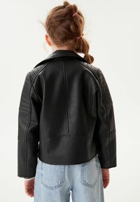 Svart fusk läder bikerjacka med quiltade axeldetaljer, som har en urtagbar krage och en figurnära design, parat med ljusblå jeans.