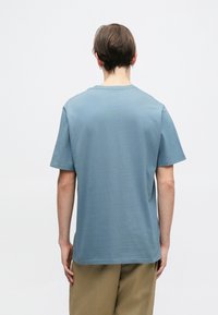 Modré bavlněné tričko s krátkými rukávy a kulatým výstřihem, s hladkou texturou. Záda jsou jednoduchá, bez viditelných log nebo grafik.