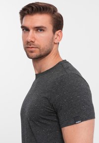 Mørkegrå kortærmet t-shirt med rund hals, fremstillet i et struktureret stof med hvide spækkelser og et lille sort mærke på ærmet.
