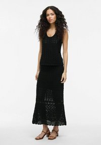 Conjunto de top sin mangas y falda de ganchillo negro, con un patrón de zigzag texturizado, que presenta un cuerpo ajustado y una falda fluida de longitud hasta la rodilla.