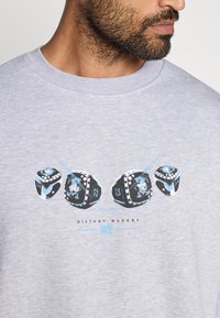 Sweatshirt cinza com uma impressão gráfica de três anéis em preto e azul, apresentando os números 22, 23 e 24, e o texto "HISTÓRIOS MARCADOS."