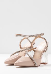 Nude lackskinnklackar med genomskinliga blockklackar, med korskorsade remmar prydda med rhinestones och spetsiga tår.