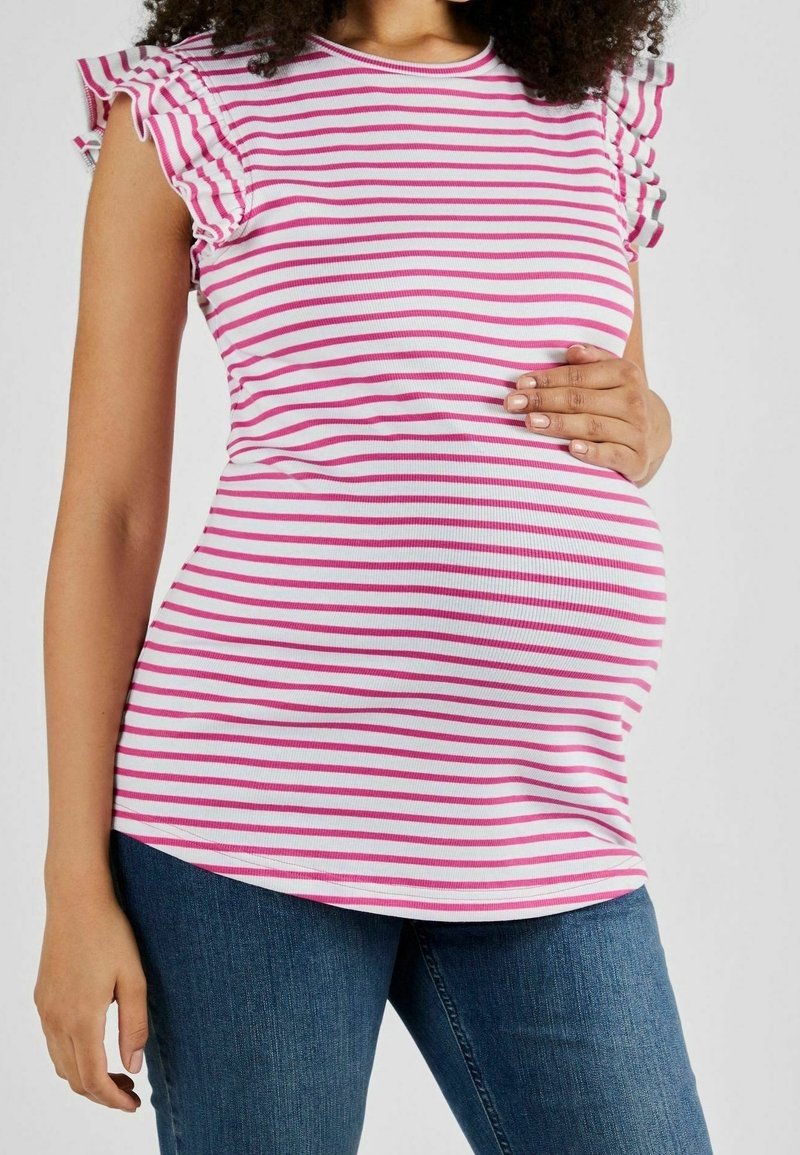 Kobieta w ciąży ubrana w różową bluzkę w białe paski z falbanami i niebieskie dżinsy, z ręką opartą na brzuchu.