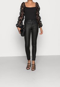 Mahón negro con mangas abullonadas de poca visibilidad y lunares, combinado con pantalones de cuero negros de cintura alta y sandalias negras de tacón alto con tiras.