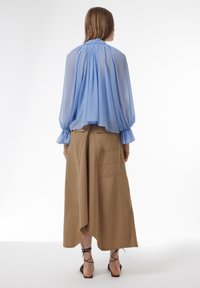 Lichtblauw doorschijnend blouse met gathered halslijn en gerimpelde manchetjes, gecombineerd met een tan hoge taille rok met zakken, gestyled met zwarte sandaaltjes met enkelband.
