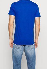 Męska niebieska koszulka z krótkim rękawem z białymi wykończeniami u rękawów i u dołu, wykonana z miękkiego materiału, z okrągłym dekoltem i dopasowanym krojem.