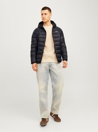 Juodas pūkinis švarkas su kapišonu, su užtrauktuku priekyje ir iškilniu raštu, dėvimas ant beige megztinio ir šviesiai mėlynų džinsų. Rudi sportbačiai.