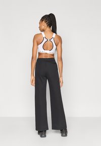 Μαύρο παντελόνι με φαρδιά μπατζάκια και λευκό αθλητικό μπουστάκι με άνοιγμα στην πλάτη και ρυθμιζόμενους ιμάντες, με λωρίδα με το λογότυπο στο κάτω μέρος.