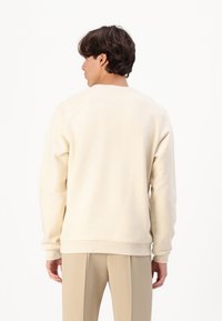 Lichtbeige sweatshirt met geribde manchetten en zoom, voorzien van een ronde halslijn en zachte textuur, gestyled met beige broeken.