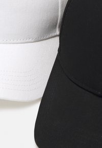 To baseballkasketter i sort og hvid. Den sorte kasket har en glat tekstur, mens den hvide kasket har et let tekstureret stof.