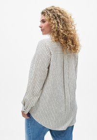 Chemise à manches longues rayée en tissu léger avec des lignes verticales noires, dotée d'un pli au dos et d'un ourlet arrondi, associée à un jean.