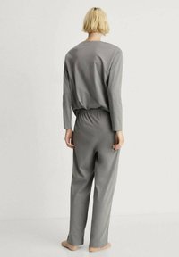 Súprava šedej loungewear pozostávajúca z trička s dlhým rukávom a nohavíc s elastickým pásom, vyrobená z mäkkého materiálu s hladkou textúrou.