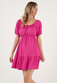 Fuchsia roze jurk met korte pofmouwen, een vierkante halslijn, een verstelbare strik aan de voorkant en een gelaagde ruffle zoom. Gemaakt van lichtgewicht materiaal.