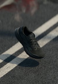 Scarpa da corsa nera con tomaia in rete, superficie testurizzata, accenti riflettenti e lacci. Suola leggera, tacco elevato e design imbottito.