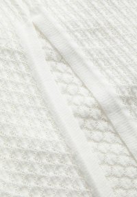 Tissu blanc texturé avec une large bande tricotée en diagonale sur un fond en maille à motifs.