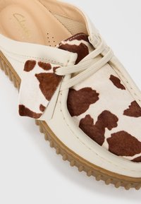 Scarpa in pelle crema con motivo in pelle di mucca marrone e bianco, lacci beige e suola in gomma spessa.
