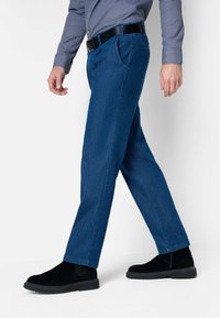 Pantalons en denim bleu avec une coupe droite, dotés de poches avant et d'une texture lisse. Associés à des bottines en daim noires.