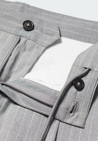 Pantaloni grigi con righe sottili, dotati di chiusura con zip e bottone. La vita presenta una texture liscia e un dettaglio interno di fodera bianca.